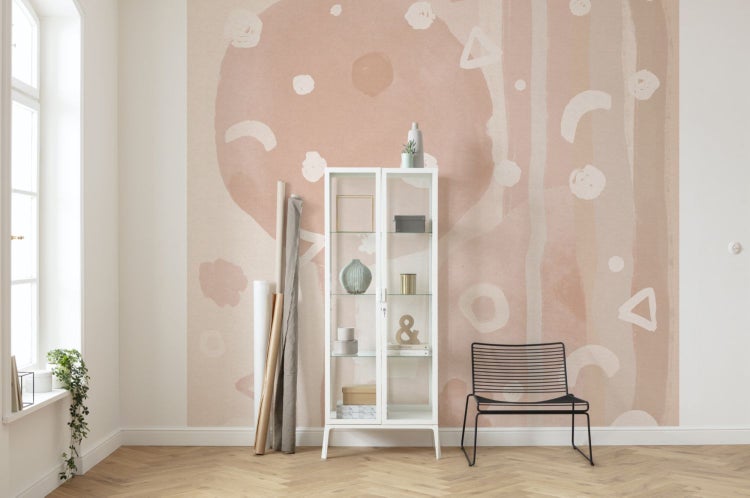 Ein Raum mit einer abstrakten Tapete in Rosatönen, einem weißen Glasschrank und einem schwarzen Stuhl.