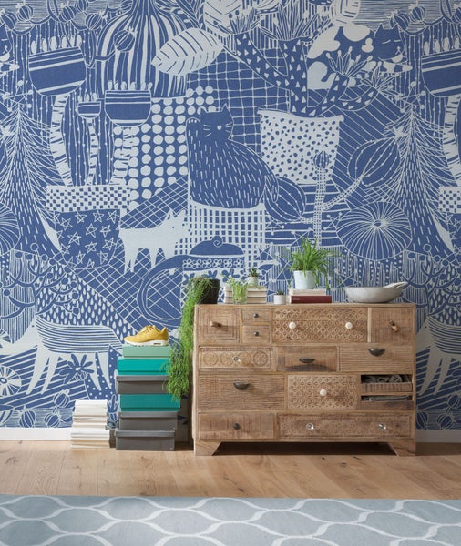 Raumansicht mit gemusterter Tapete, Holzkommode und Dekorationsgegenständen