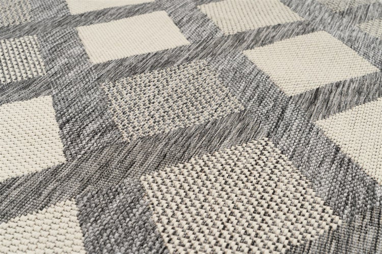 Gewebter Teppich mit geometrischem Muster in Grau und Weiß und strukturierter Oberfläche.