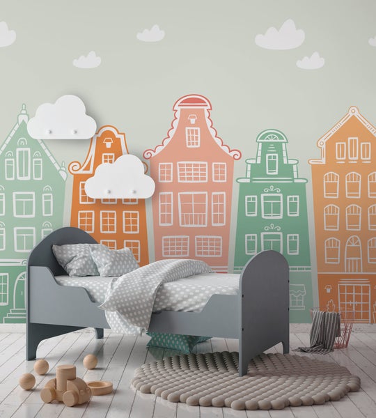 Fototapete für Kinderzimmer mit bunten Giebelhäusern und Wolken in einer Zimmerszene mit grauem Kinderbett und Holzspielzeug auf weißem Boden.