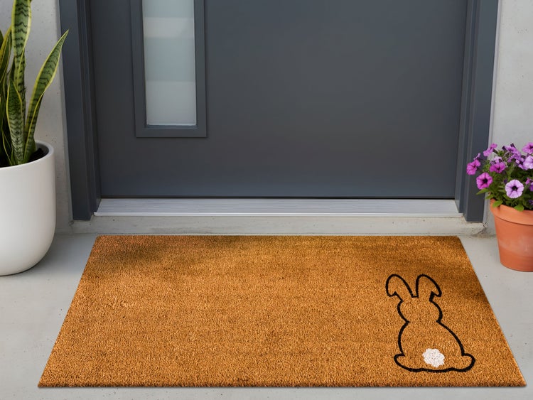 Rechteckige Kokos-Fußmatte mit schwarzer Hasen-Silhouette und weißem Detail vor einer grauen Haustür im Außenbereich.