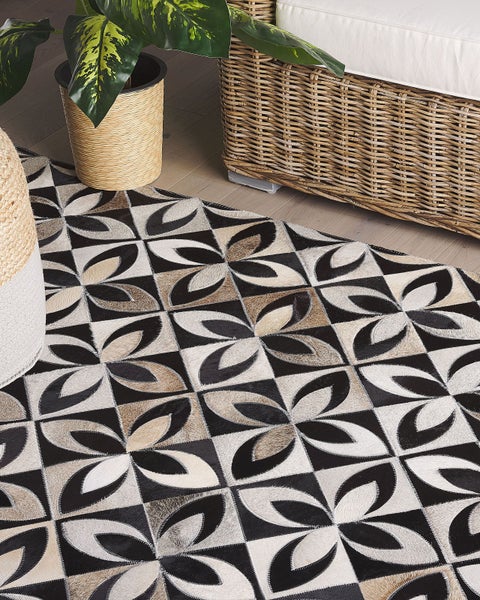 Patchwork-Teppich aus Kuhfell mit geometrischem Blütenmuster im Wohnzimmer neben einem Korbsessel und einer Pflanze.