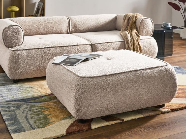Hocker und Sofa aus Bouclé-Stoff im hellen Wohnzimmer auf einem gemusterten Teppich.