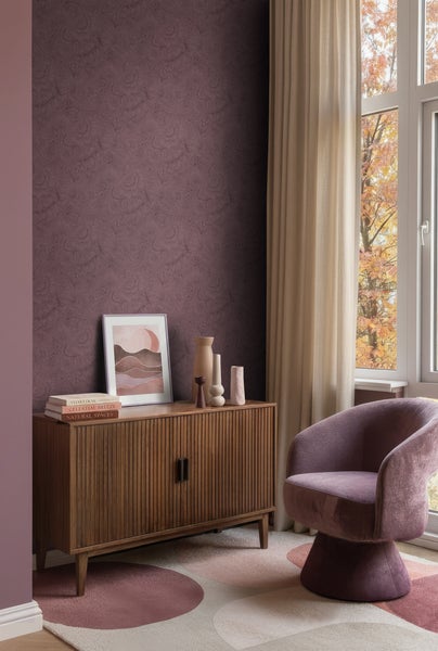 Heller Wohnbereich mit gemusterter Tapete, einem Sideboard aus Holz mit Dekoration, einem Sessel und einem Fenster mit Vorhängen.