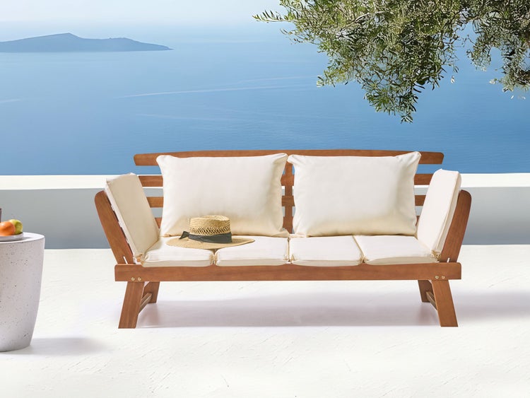 Holzgartenbank mit Polstern und Strohhut vor Meereshintergrund