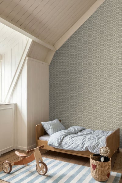 Kinderzimmer mit gemusterter Tapete, Holzbett mit gestreifter Bettwäsche, Holz-Laufrad und gestreiftem Teppich im hellen Dachgeschoss.