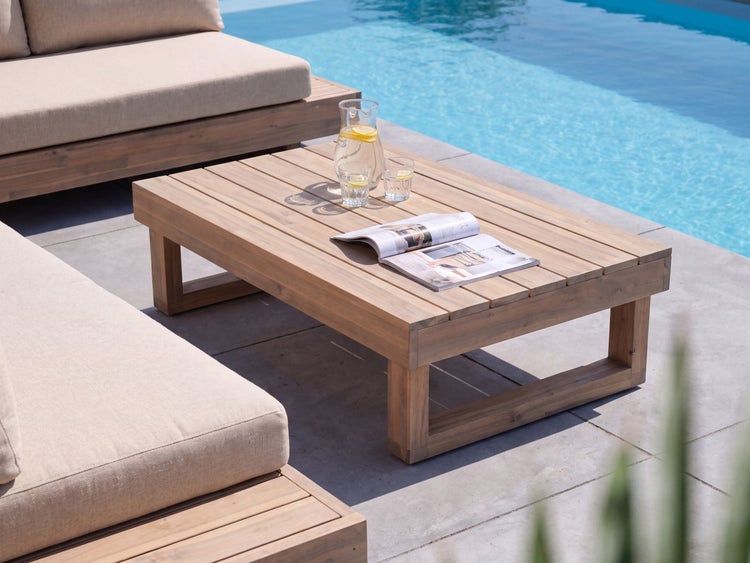 Niedriger Gartenloungetisch aus Holz mit aufgeschlagenem Magazin und Glaskaraffe auf einer Terrasse am Pool mit Loungemöbeln
