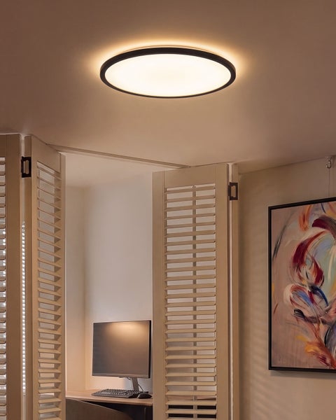 Moderne runde LED Deckenleuchte montiert an einer hellen Zimmerdecke in einem Wohnbereich mit Lamellentüren und abstraktem Wandbild.