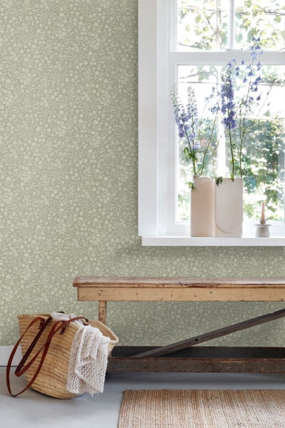 Vliestapete mit floralem Muster in einem hellen Raum mit Holzbank und Fenster.