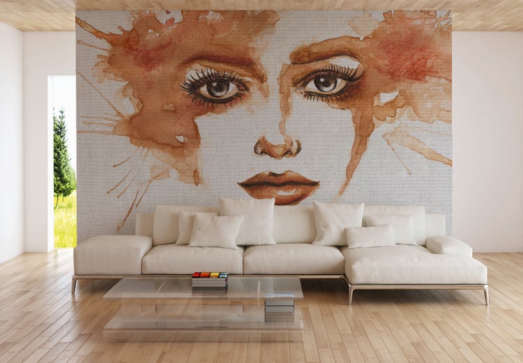 Großflächige Fototapete mit einem künstlerischen Frauenporträt in Aquarell-Optik hinter einem Sofa im Wohnzimmer mit Parkettboden.