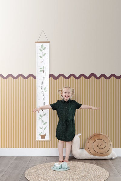 Mädchen steht neben einer Wachstumstabelle mit Eichenmotiv und einem Schneckenkissen in einem Kinderzimmer