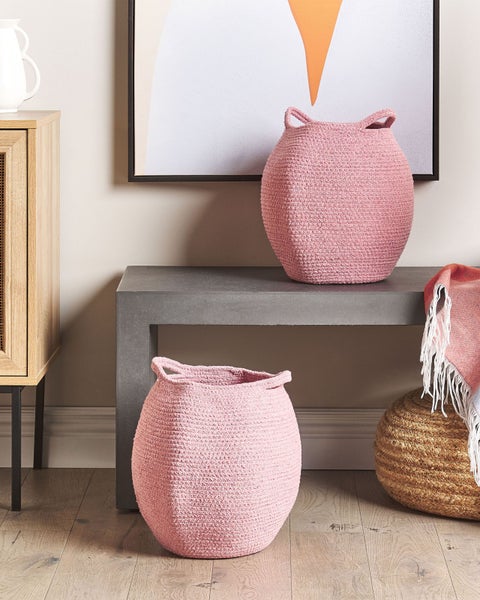 Zwei rosa geflochtene Aufbewahrungskörbe mit Griffen in einem modernen Wohnzimmer mit Betontisch und Jutepouf.
