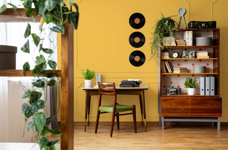 Organisierter Vintage-Arbeitsbereich mit Holzschreibtisch, Schreibmaschine, Stuhl und Bücherregal vor einer Wand mit Zierleisten und Schallplatten.