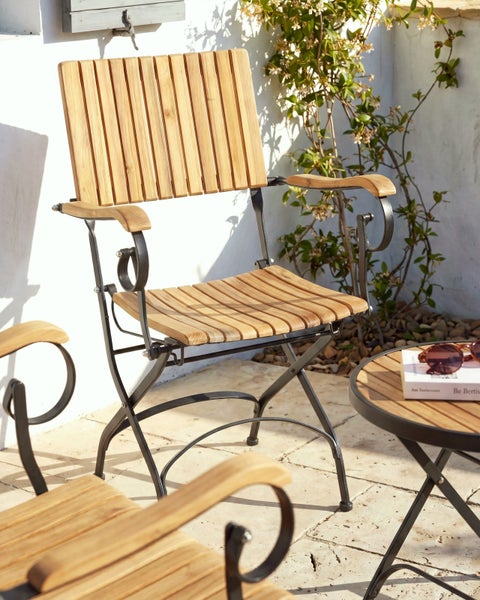Gartenstuhl mit Holzlatten und schwarzem Metallgestell auf einer sonnigen Terrasse neben einem Beistelltisch.