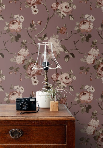 Eine Person verwendet eine Smartphone-App, um verschiedene Tapetenmuster in einem Raum mit einem Klavier und Pflanzen zu visualisieren.