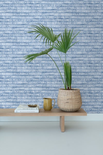 Zimmerpflanze in einem Korb auf einem Holztisch mit Dekoration vor einer gemusterten Tapete
