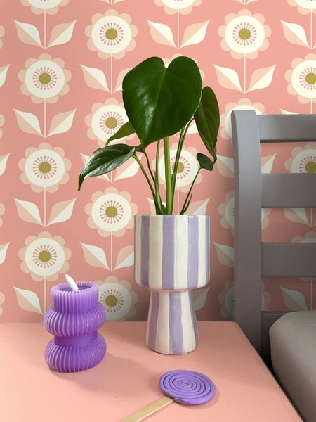 Dekorative Szene mit Zimmerpflanze in gestreiftem Topf, gewellter Kerze und floraler Tapete