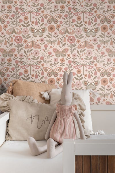 Tapete mit Blumen- und Schmetterlingsmuster, Stofftierhase und Kissen auf einem Kinderbett