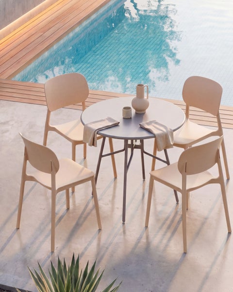 Modernes Gartenmöbel-Set mit rundem Tisch und vier Stühlen auf einer hellen Terrasse neben einem Swimmingpool.
