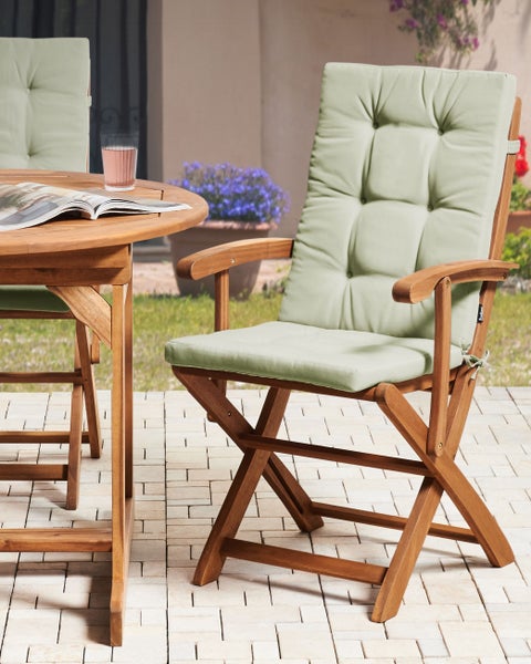 Gartenmöbel-Set aus Holz mit Klappstühlen, hellgrünen Polstern und rundem Tisch auf einer hellen, gepflasterten Terrasse.