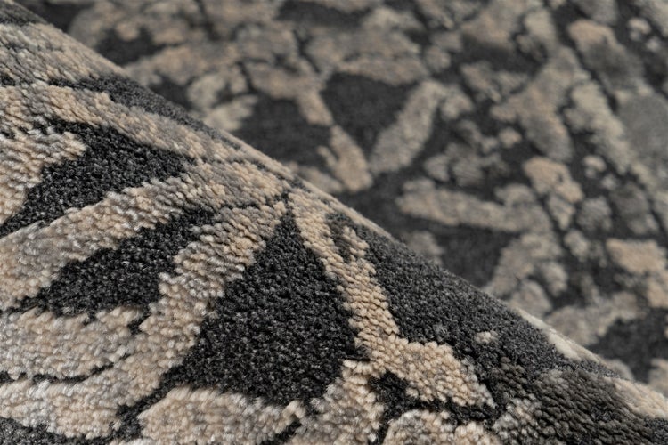 Nahaufnahme eines strukturierten Teppichs mit abstraktem anthrazit-beigem Muster und dichtem Flor.
