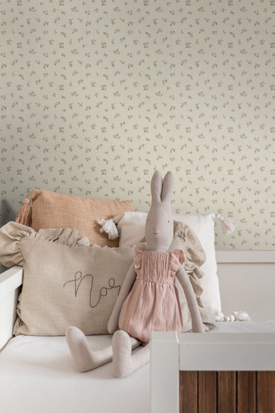 Tapete mit kleinem Blumenmuster in einem Kinderzimmer hinter einem weißen Bett mit Dekokissen und einem Stoffhasen.