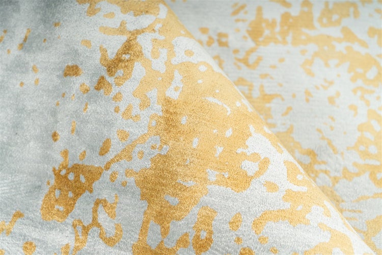 Detailansicht eines Teppichs mit abstraktem Muster in Gold und Grau sowie einer weichen Oberfläche.