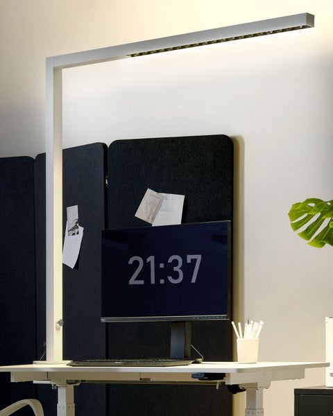 Moderner Arbeitsplatz mit Schreibtischlampe, Computermonitor und Büromaterialien.