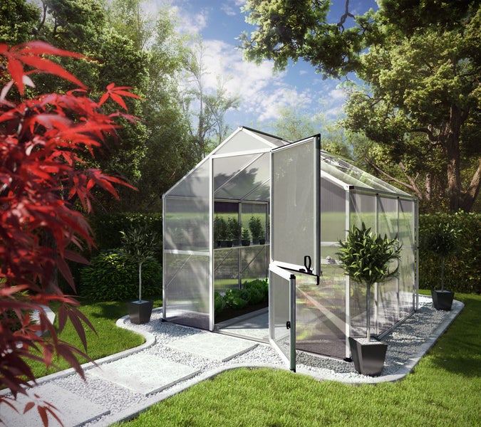 Großes Gewächshaus aus Aluminium mit Polycarbonatplatten und geöffneter Stalltür in einem Garten mit Steinweg und Bäumen.
