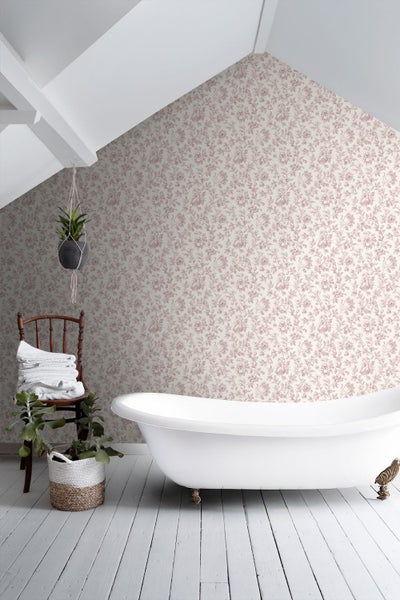 Helles Badezimmer mit Blumenmuster-Tapete, einer freistehenden Badewanne und einem Holzstuhl mit weißen Handtüchern unter einer Dachschräge.