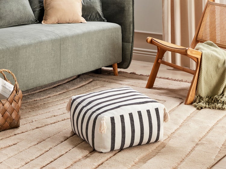 Wohnszene mit Sofa, Holzstuhl, Teppich und gestreiftem Sitzhocker