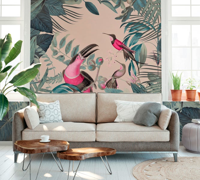 Fototapete Tropen mit Tukan, Kolibris und Palmblättern in einem hellen Wohnzimmer mit beigem Sofa und Holztischen.
