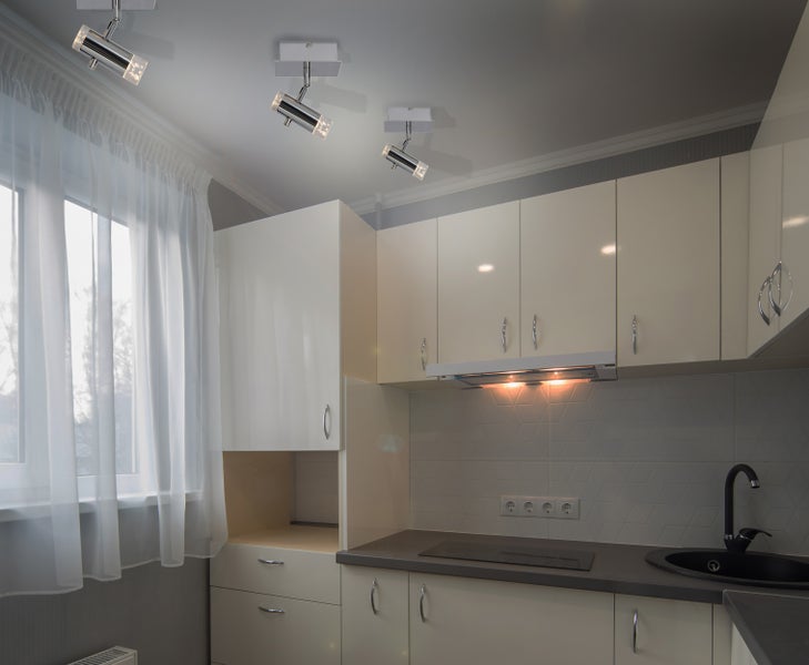 Helle Küche mit Oberschränken, Spüle, Kochfeld und Deckenleuchten.