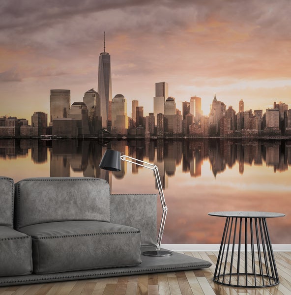 Fototapete mit der Skyline von New York City bei Sonnenuntergang und dem One World Trade Center in einem modernen Wohnzimmer mit grauem Sofa.