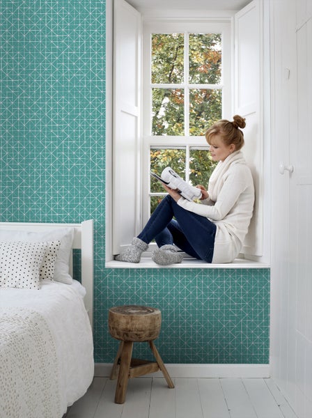 Gemütliches Zimmer mit geometrischer Tapete, Fensterplatz mit Lesender, Bett und Hocker