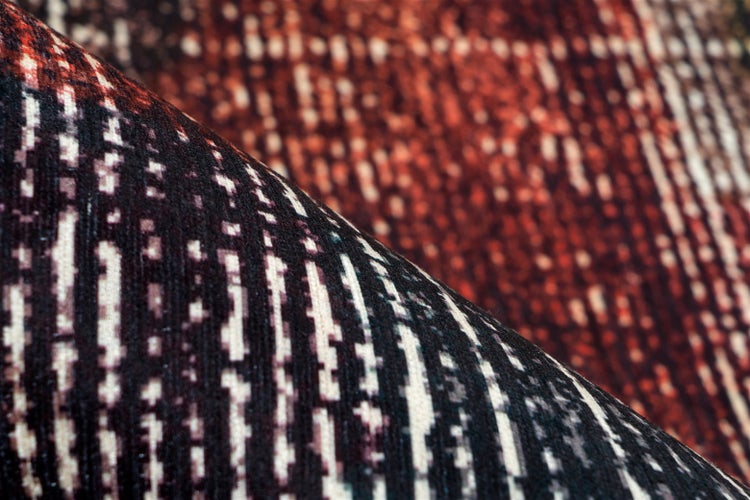 Nahaufnahme eines gewebten Teppichs mit strukturierter Oberfläche und einem gepixelten Muster aus vertikalen Streifen.