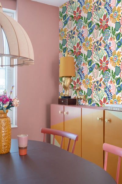 Wandgestaltung mit bunter Vliestapete im floralen Muster neben einer rosa Wand und einem Sideboard.