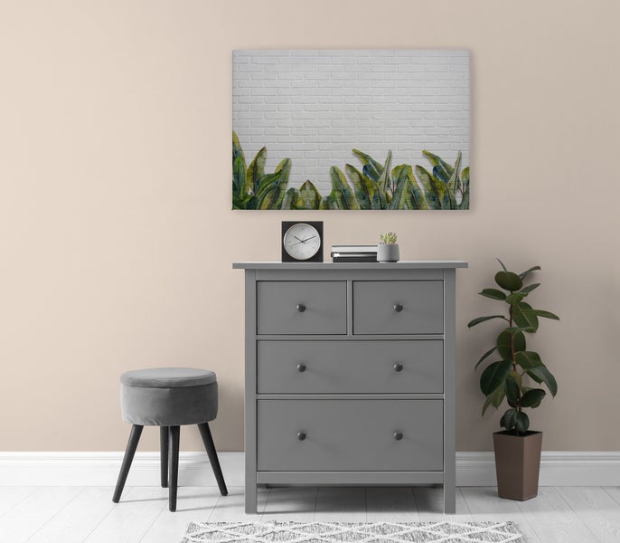 Moderne Kommode mit vier Schubladen in einem stilvoll eingerichteten Wohnraum mit Wandbild, Hocker und Zimmerpflanze.
