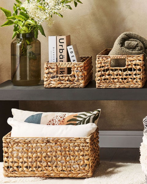 Geflochtene Aufbewahrungskörbe aus Naturfasern in einer Wohnzimmerszene mit Büchern, einer Decke und Kissen.