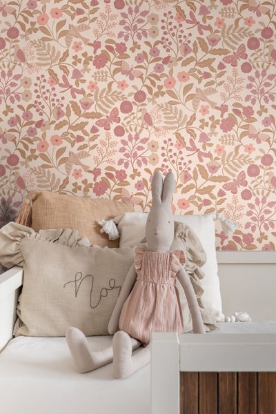 Tapete mit Blumenmuster, Vögeln und Schmetterlingen in einem Kinderzimmer hinter einem Bett mit Kissen und einem Plüschhasen.