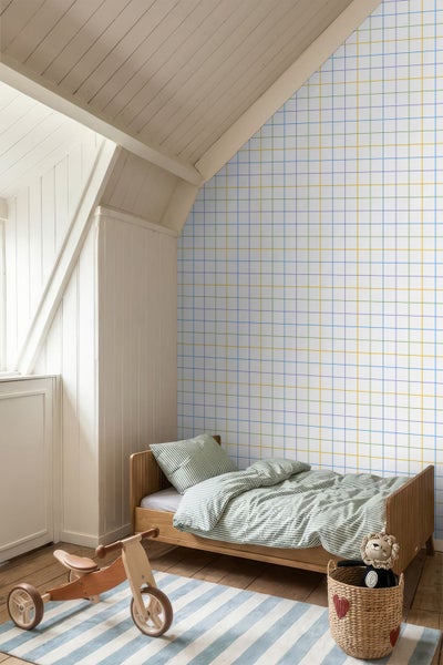 Kinderzimmer unter einer Dachschräge mit Vliestapete im Karomuster mit bunten Linien, einem Holzbett und hellem Dielenboden.