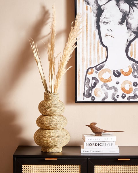 Dekoratives Stillleben mit Vase, Trockenblumen, Bild und Dekorationsobjekt auf einem Schrank