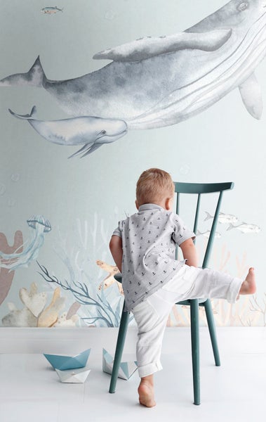 Ein Kind klettert auf einen Stuhl vor einer Wandtapete mit Meeresmotiven und Walen.