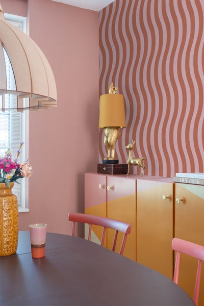 Esszimmer mit Esstisch, Stühlen, Kommode, Lampe und Blumenvase in einem Wohnraum mit Wellentapete