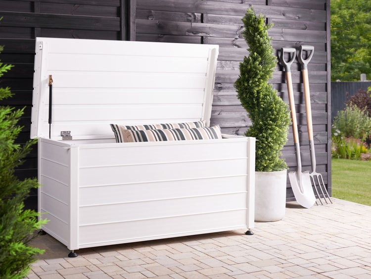 Geöffnete, weisse Gartenbox mit Kissen, Schaufel und Gabel auf einer Terrasse