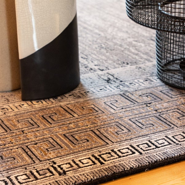 Teppich mit Mäander-Muster und griechischem Schlüssel-Design in einem Wohnraum mit Vase und Metalltisch.