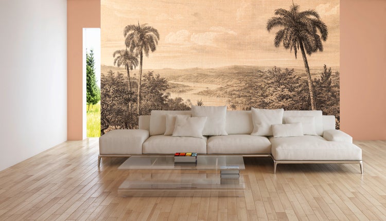 Wohnzimmer mit Fototapete einer tropischen Landschaft mit Palmen, hellem Ecksofa, Glastisch und Parkettboden.