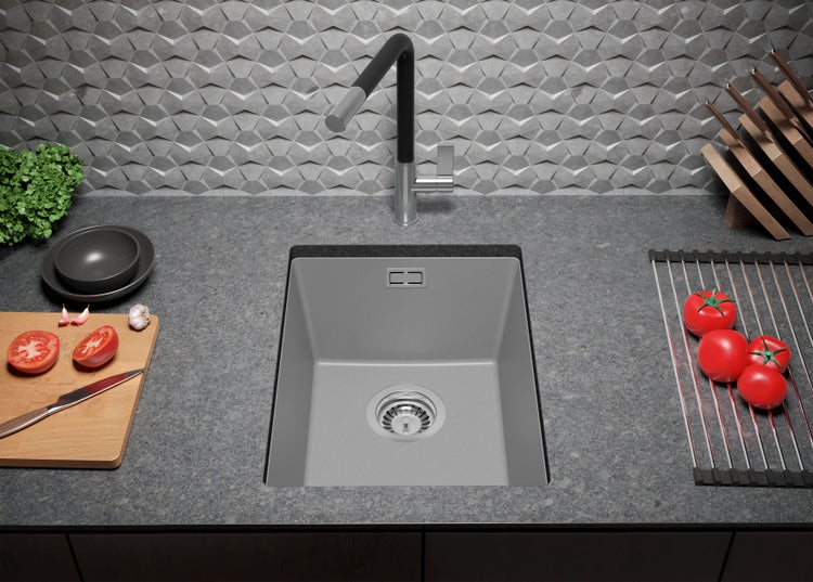 Küchenspüle mit Abtropffläche, Armatur, Schneidebrett und Tomaten auf einer Küchentheke vor einer grauen Wand