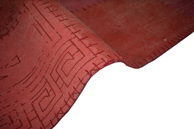 Patchwork-Teppich mit geometrischen Mustern und Symbolen in verschiedenen Rottönen.