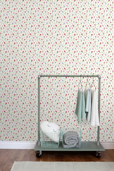 Blumentapete mit Kleiderständer, Körben und Dekokissen in einem Zimmer.